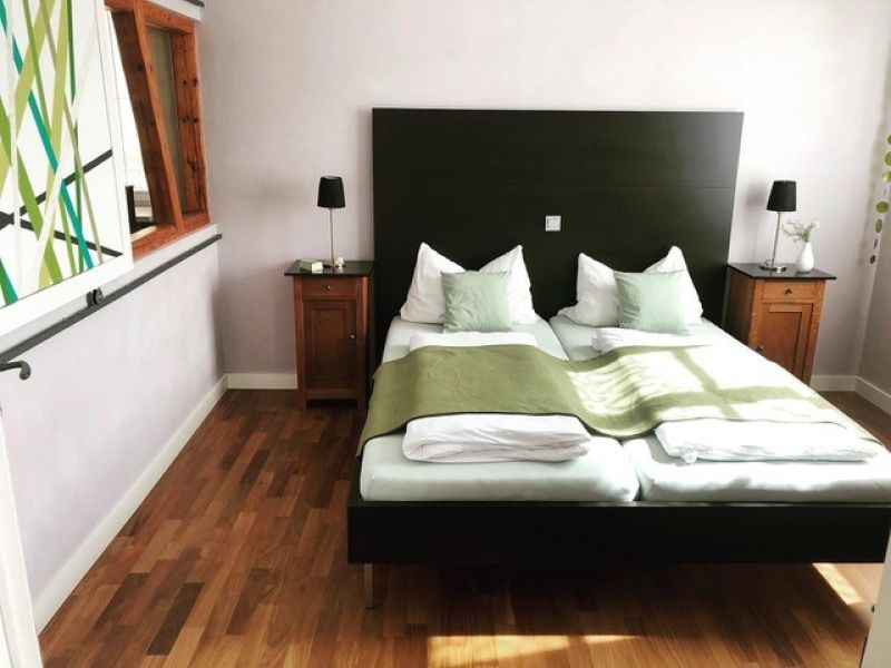 Schlafzimmer 1 mit Doppelbett, grünen Decken und Holzboden