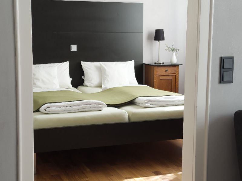 Schlafzimmer 1 mit Doppelbett, Nachttisch und Blick durch die Tür